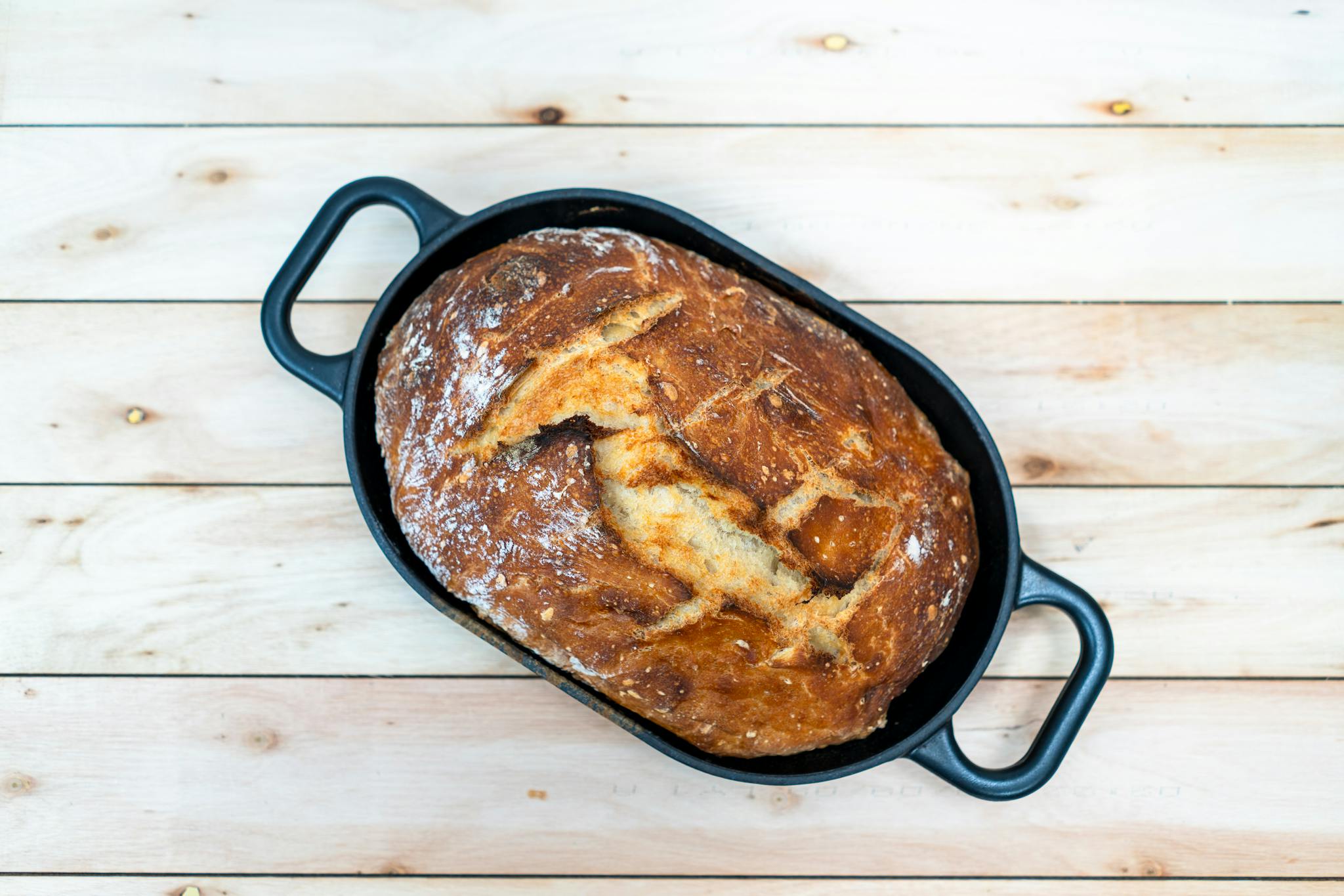 Top view of a homemade sourdough loaf in a Dutch oven, resting on a wooden surface.